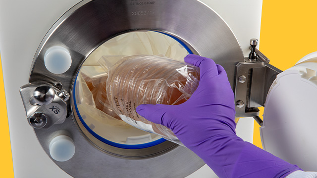 <p>Navigating Cleanroom Compliance for Safe Material Transfer</p>
A close-up image of a gloved hand placing a sealed petri dish into a circular opening of a laboratory device. The device features a metal rim and a bright blue background, emphasizing a sterile and controlled environment for scientific work.