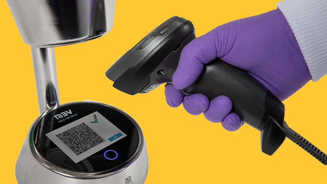 <p>Getting Equipped for the Future of Air Monitoring</p>
A close-up image of a hand wearing a purple glove holding a barcode scanner aimed at a circular device displaying a QR code. The background is a vibrant blue, enhancing the focus on the scanning action and the technology being used.