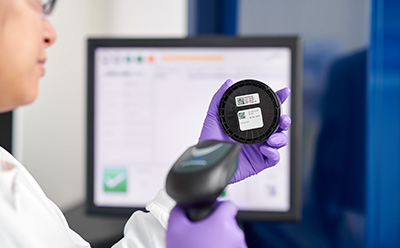 A laboratory technician using a barcode scanner on a sample container, showcasing digital data management and automated recordkeeping for improved accuracy and audit-ready reporting.