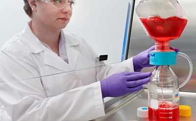 <p>Mastering Media Preparation</p>
Photograph of a scientist using a Steritop® E filter unit to filter cell culture media in the tissue culture hood.