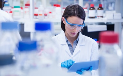 Chemist wearing safety glasses and using tablet pc in lab testing for Coronavirus Covid19 vaccine.