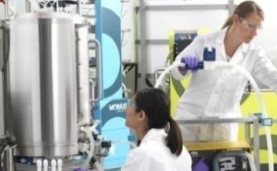 Two scientists work to the right of a bioreactor