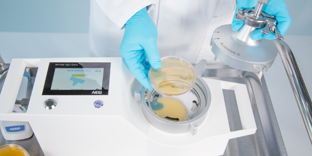 <p>Muestreo microbiano de gases comprimidos</p> Un trabajador con guantes azules introduce una placa de cultivo en un dispositivo de muestreo microbiano de gas comprimido.