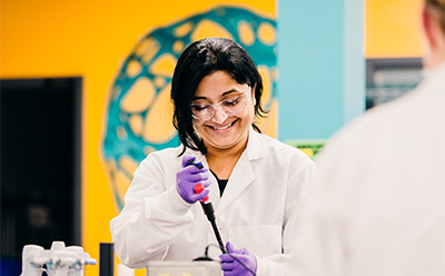 Scientist smiling while using a micropipettor to pipet in the lab.