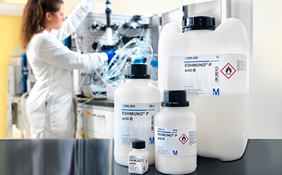 Affinity Chromatography with Eshmuno<sup>®</sup> Resins A scientist in a lab coat working with equipment and chemicals in a laboratory setting. In the foreground, there are three chemical containers with labels, two are large and one is smaller, marked with hazard symbols for flammable and corrosive substances.