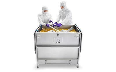 Two people in protective lab attire are interacting with the contents of a large metal container. The container has latches on the side, indicating it may has a lid. 