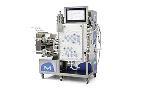 Chromatography Systems Chromatograph system for bioprocessing, featuring various tubes, dials, and components, predominantly silver with blue accents and a logo featuring the letter ‘M’ on the side panel.
