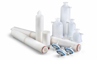 A white capsule and cartridge filters of different sizes. On left, lying down are 20 and 30 inch cartridge filters, with smaller cartridge filters standing upright. Capsules are standing upright on right side of image. while front center shows smaller white OptiScale® 47 capsules.