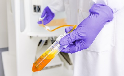 NovaSeptum® SURe Sampling C-Flex® tubing A laboratory worker wearing purple gloves holds a NovaSeptum® SURe Sampling Assembly with transparent tubing and orange fluid in a single-use processing environment.