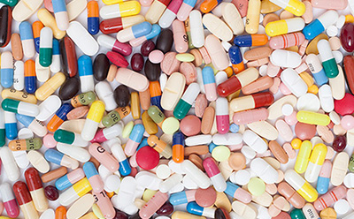 A diverse collection of pharmaceutical pills and capsules. They come in various shapes and colors, including pink, yellow, white, blue, and red. Some capsules are clear or opaque with different colored ends.