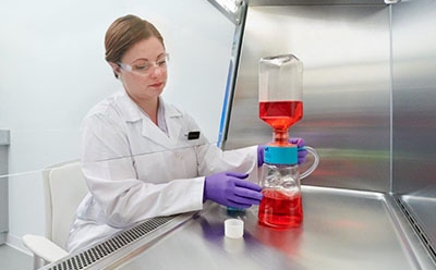 Millipore® Sterile Filters The image show a woman in a white lab coat, working with laboratory flask containing a red liquid, which is connected to another piece of equipment with blue liquid at the bottom.