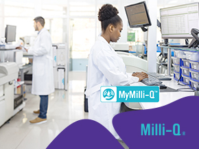 A bright laboratory scene with scientists at work. In the foreground, a female lab technician in a white coat sits at a workstation, facing a computer monitor. In the background, other staff member in lab coats work at benches with equipment.