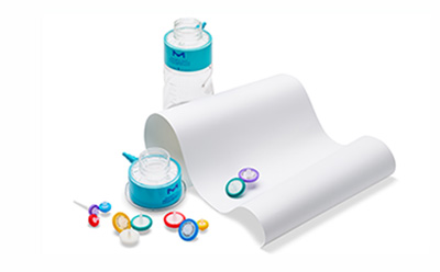 Millipore® membranes Product image of a membrane filter roll beside a laboratory bottle and assorted colored filter components on a white background.