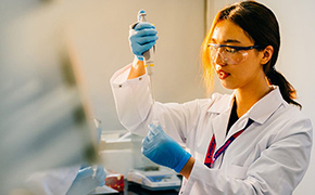 Protein Sample Preparation Dark-haired female scientist wearing in blue nitrile gloves, white lab coat, and safety goggles pipettes solution into a centrifugal tube