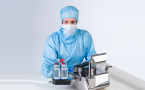 Sterility Testing Equipment for Microbiological QC Five scientists wearing white lab coats, safety goggles and blue nitrile gloves work at different stations within the lab operating chemistry analytical instruments and filling glass beakers and vials.