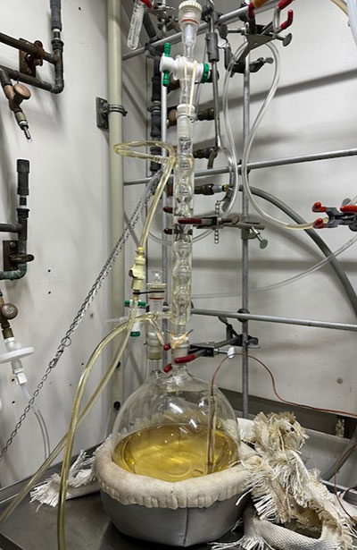Round-bottom flask 実験台に載せられた丸底フラスコから、あらゆる方向にチューブが出ている。中の液体は薄い黄色である。