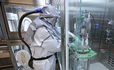 HPAPI manufacturing Scientist in full PAPR protective suit operating a glass bioreactor inside a containment isolator for highly potent API (HPAPI) small-molecule manufacturing