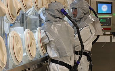 Lipid particle formulation Pharmaceutical technician in grey PAPR suit operating a Howorth Air Tech isolator glove box for lipid particle (LP) drug delivery formulation manufacturing