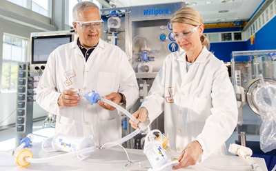Technical specialists preparing single-use assemblies with tubing and connectors in an aseptic processing environment.