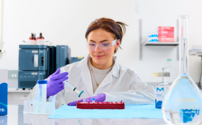 Scientist filtering a sample for HPLC analysis Female scientist in white coat and purple gloves using a Millex PES syringe filter to filter sample into a vial on the benchtop, with glassware on the bench and HPLC in background
