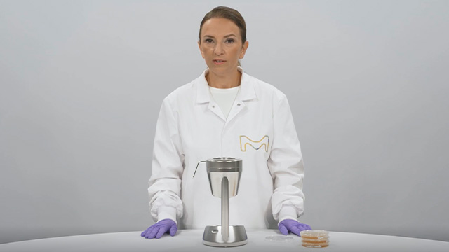 <p>Muestreador de aire microbiano MAS-100 Sirius®</p> Científico con bata blanca de laboratorio y guantes morados, de pie junto a una mesa de laboratorio