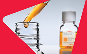 A close-up image of a glass pipette dispensing a yellow liquid into a clear glass container. In the background, there is a small bottle with a white cap and a label, partially visible. The image features a red triangular design element on the left side.