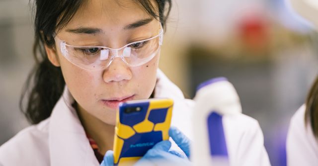 Digital Direct Quote Laboratory researcher wearing safety glasses and gloves using a smartphone while working in a laboratory.