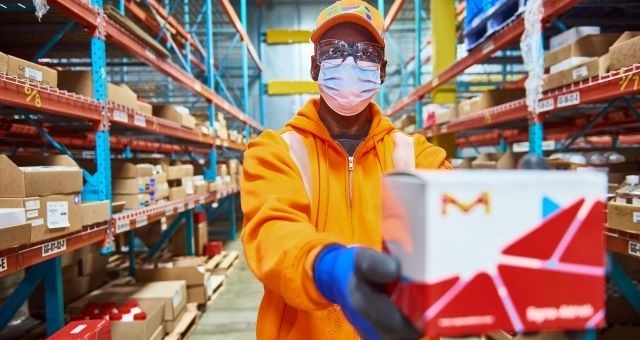 Digital Direct Availability Distribution center employee handling a shipment box in a warehouse with stocked shelving.