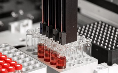 Reaction optimization Primer plano de un sistema de automatización de laboratorio con varias puntas de pipeta colocadas sobre diversos viales de vidrio que contienen líquido rojo.