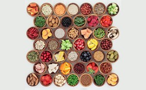 a top-down view of a neatly arranged grid of small wooden bowls, each containing different natural food ingredients.