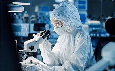 Pyrogen Testing Webpage Picture A scientist wearing full PPE observes a sample on a microscope.