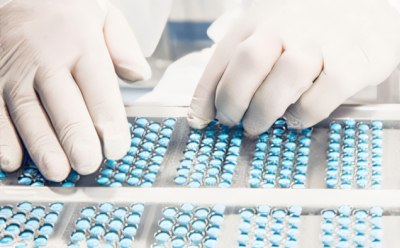 Pill inspection Instalación de fabricación farmacéutica o médica. Muestra a una persona en ropa protectora manipulando bandejas llenas de cápsulas azules.