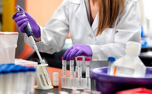 Mujer con bata de laboratorio , guantes de seguridad y gafas de seguridad, trabajando en un laboratorio.