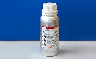 The image features a metallic silver bottle with a white screw-on cap, positioned vertically on a smooth white surface. The bottle is labeled with detailed information, including safety symbols indicating flammability and toxicity, along with written instructions in black and red text. The label includes the name "Sigma-Aldrich" prominently displayed in red. Behind the bottle, there is a vibrant blue background that contrasts sharply with the silver and white of the bottle. The overall composition highlights the bottle as the focal point, emphasizing its importance in a laboratory setting related to liquid electrolyte research and development.