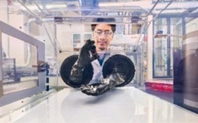 A scientist wearing safety goggles and a lab coat is working inside a glove box in a high-tech laboratory. The researcher is using gloved hands through the glove ports to handle a material inside the controlled environment. The background showcases advanced lab equipment and an industrial setting, emphasizing precision and safety in handling sensitive materials