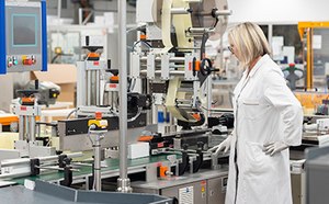 Contract Manufacturing for IVD, Medical Device, and Biologicals Woman in a labcoat and goggles inspecting a lateral flow membrane manufacturing line.
