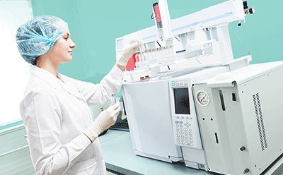 Researcher putting vial in Gas Chromatography instrument Female scientific researcher with lab coat, gloves and hair protection placing vial flask in gas chromatography instrument
