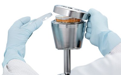 A close-up of a magnetic stainless steel lid with a handle being removed from a microbial air sampler, showing a 90 mm settle plate inside. A close-up of a magnetic stainless steel lid with a handle being removed from a microbial air sampler, showing a 90 mm settle plate inside.