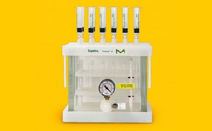 Dispositivo de filtración de laboratorio con una base blanca y cinco tubos transparentes colocados en vertical en la parte superior. Los tubos están llenos de líquido y tienen marcas verdes. En la parte delantera del aparato se ve un manómetro que indica la presión del sistema. El fondo es de color amarillo brillante, lo que aumenta la visibilidad del equipo.