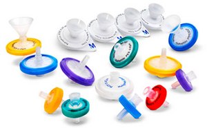 Un surtido de filtros de jeringa Millex<sup>®</sup> en varios colores y tamaños, mostrados sobre un fondo blanco. Estos filtros representan una gama de opciones de filtración de pequeño volumen para uso en el laboratorio. Los filtros vienen en diferentes colores como azul, verde, amarillo, morado y rojo, que indican diferentes tipos de filtros o tamaños de poro. Cada filtro tiene forma circular con una estructura cónica en forma de embudo en la parte superior para unirse a una jeringa. La parte central de los filtros es blanca con una etiqueta que incluye la marca “Millex®”. Algunos filtros tienen una sección superior transparente mientras que otros son opacos. En la imagen se muestra también un embudo accesorio, que se utiliza para ayudar a verter líquidos en el filtro. Estos filtros establecen el estándar en la filtración de pequeño volumen (1-200 ml), y su uniformidad insuperable en la preparación de la muestra ha llevado al desarrollo de muchos métodos que especifican su uso.
