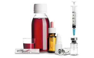 Varios envases de medicamentos líquidos y herramientas de aplicación sobre fondo blanco. Hay un frasco rojo de jarabe para la tos con un vaso medidor, un cuentagotas ámbar más pequeño, un vial medicinal transparente y una jeringuilla que inyecta líquido en otro frasco.
