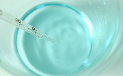 Biological buffer solution in beaker Imagen de una disolución tampón biológica de color azul claro en un vaso de precipitado con una pipeta.