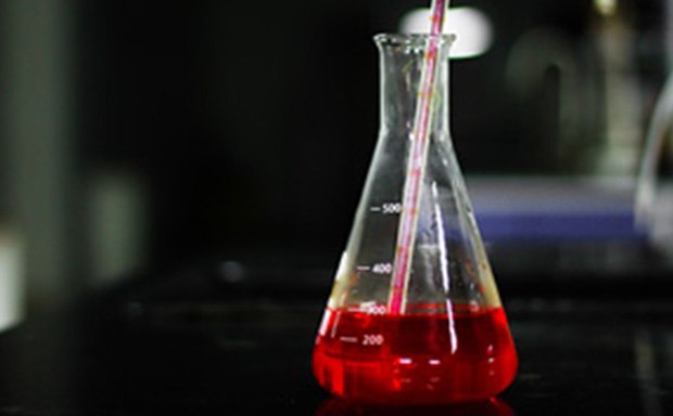 Media for cell culture Se está vertiendo un líquido rojo en un matraz Erlenmeyer aforado, con graduaciones en 200, 300 y 500 mililitros, sobre una encimera oscura de laboratorio.