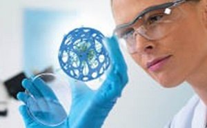 Cient&iacute;fico con bata de laboratorio y guantes azules est&aacute; examinando un detallado modelo azul en 3D de una estructura molecular con equipos de laboratorio borrosos en el fondo.