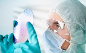 Científico que lleva ropa protectora inspeccionando el sustrato prefabricado de dispositivo electrónico preestampado
