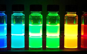 Seis viales de vidrio con líquidos de colores brillantes, azul, verde, amarillo y rojo, sobre un fondo oscuro