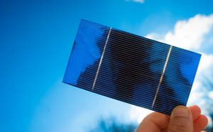 Fina célula solar azul sostenida por una mano a la luz solar.