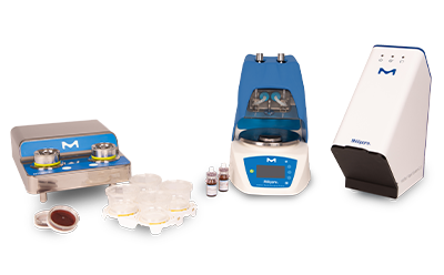 Tres equipos de laboratorio asociados al sistema Milliflex® Rapid 2.0. A la izquierda, hay una unidad de acero inoxidable con dos plataformas circulares, cada una de las cuales sostiene una placa de Petri transparente con un medio rojo en su interior, y varias otras placas de Petri apiladas a su lado. En el centro, hay un dispositivo azul más grande con una pantalla digital y botones de control; parece una incubadora o un analizador con una puerta abierta que deja ver los componentes internos. A la derecha de la imagen se observa un dispositivo blanco.