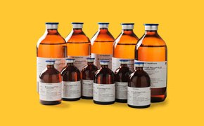 Conjunto de botellas de vidrio ámbar de varios tamaños, etiquetadas con texto blanco y azul, sobre un fondo amarillo.