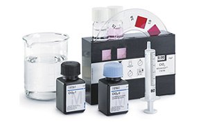 La imagen muestra un conjunto de equipos de laboratorio, como un vaso de precipitados, dos botellas de productos químicos con las etiquetas “M” y “OH”, una jeringa y tiras indicadoras de pH, lo que sugiere una configuración de laboratorio de química.
